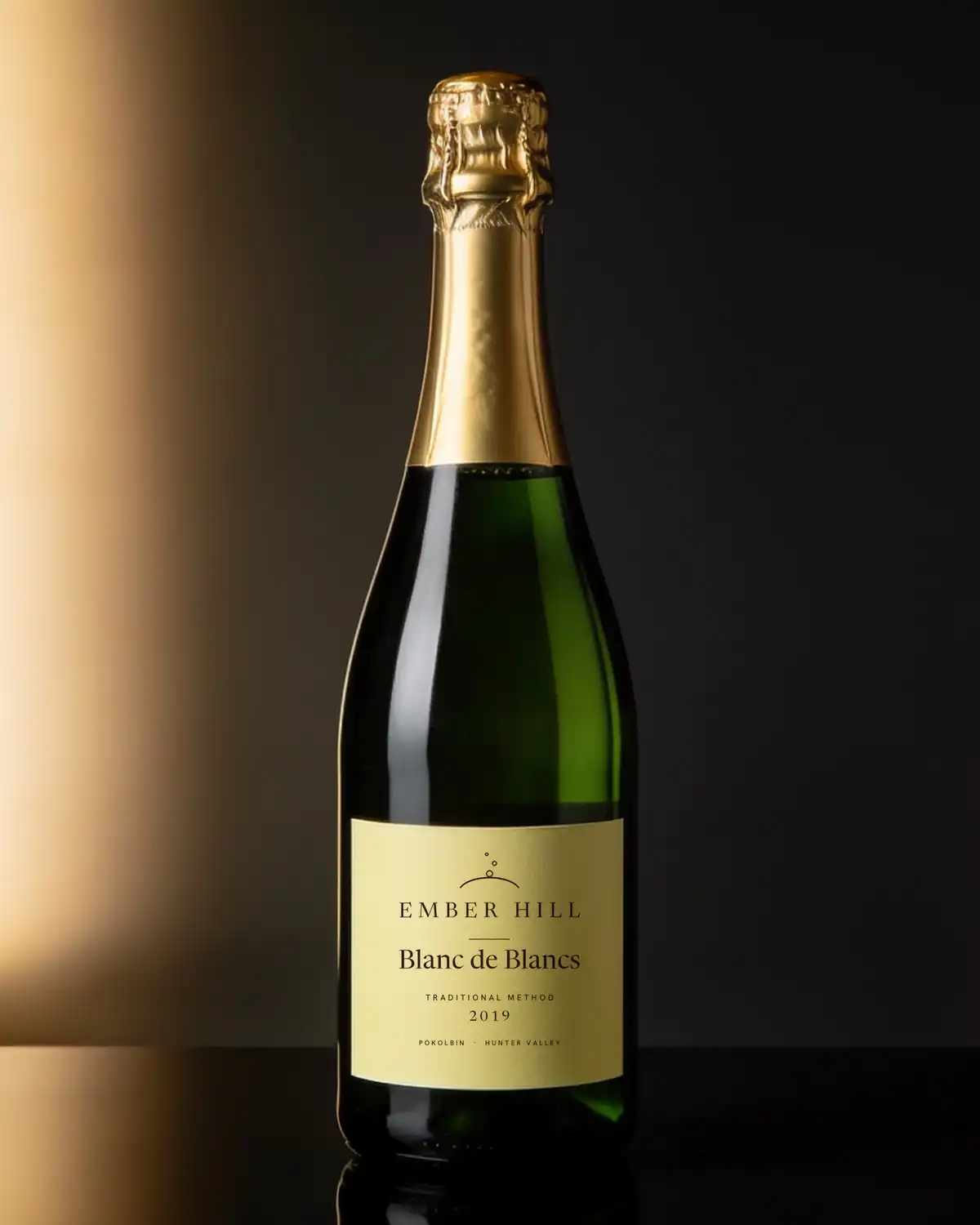 A bottle of Ember Hill Blanc de Blancs with a cream label on a dark table