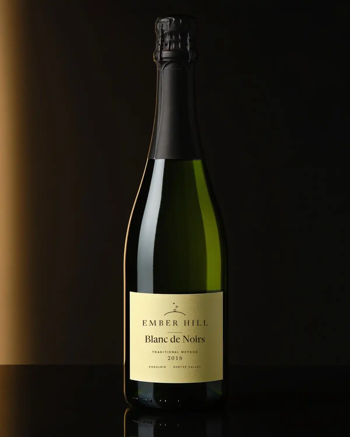 A bottle of Ember Hill Blanc de Noirs 2018, cream label, on a dark table