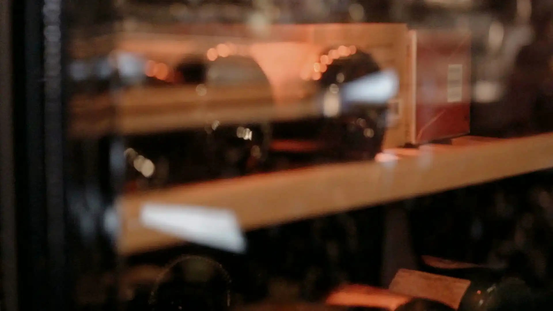 Wine bottles lying on softly lit shelves, seen out of focus through glass