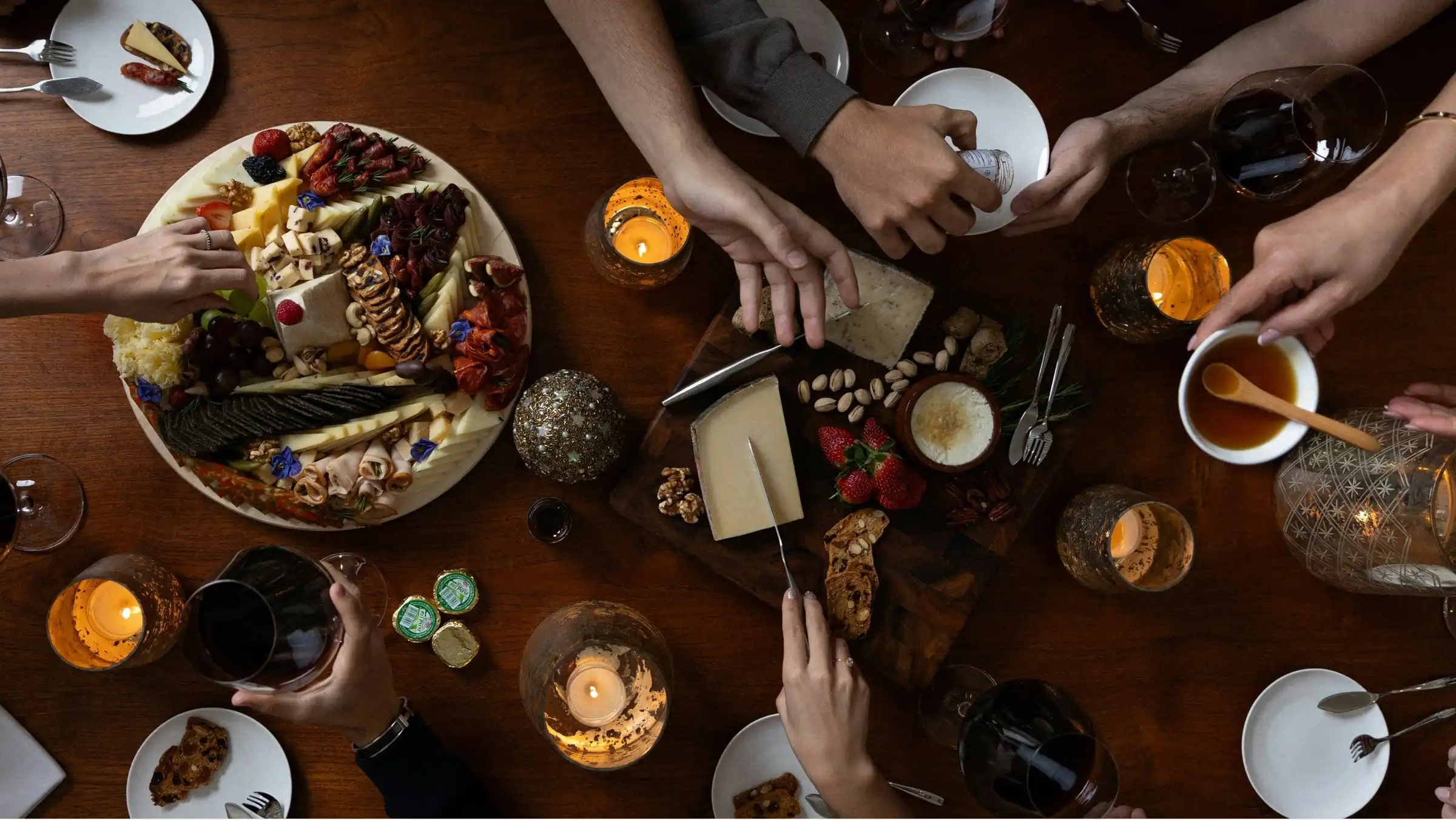 An overhead view of cheeses, fruit and bread spread across a dark table
