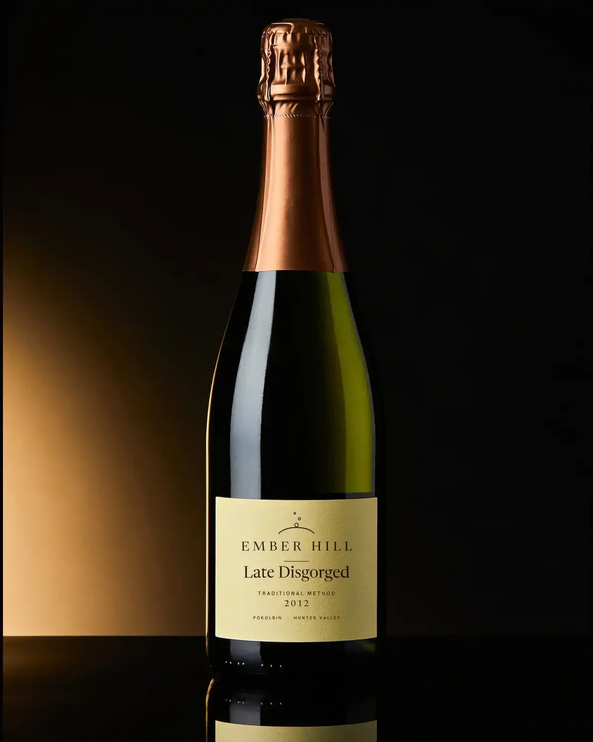 A bottle of Ember Hill Late Disgorged with a cream label on a dark table