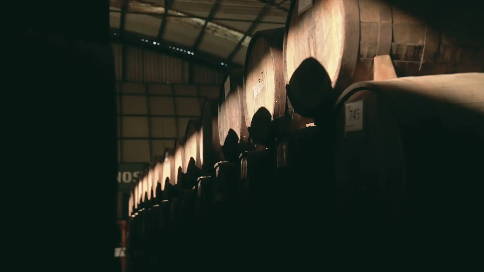 Barrels in a dark cellar, bottles resting on their sides, then a bottle being opened
